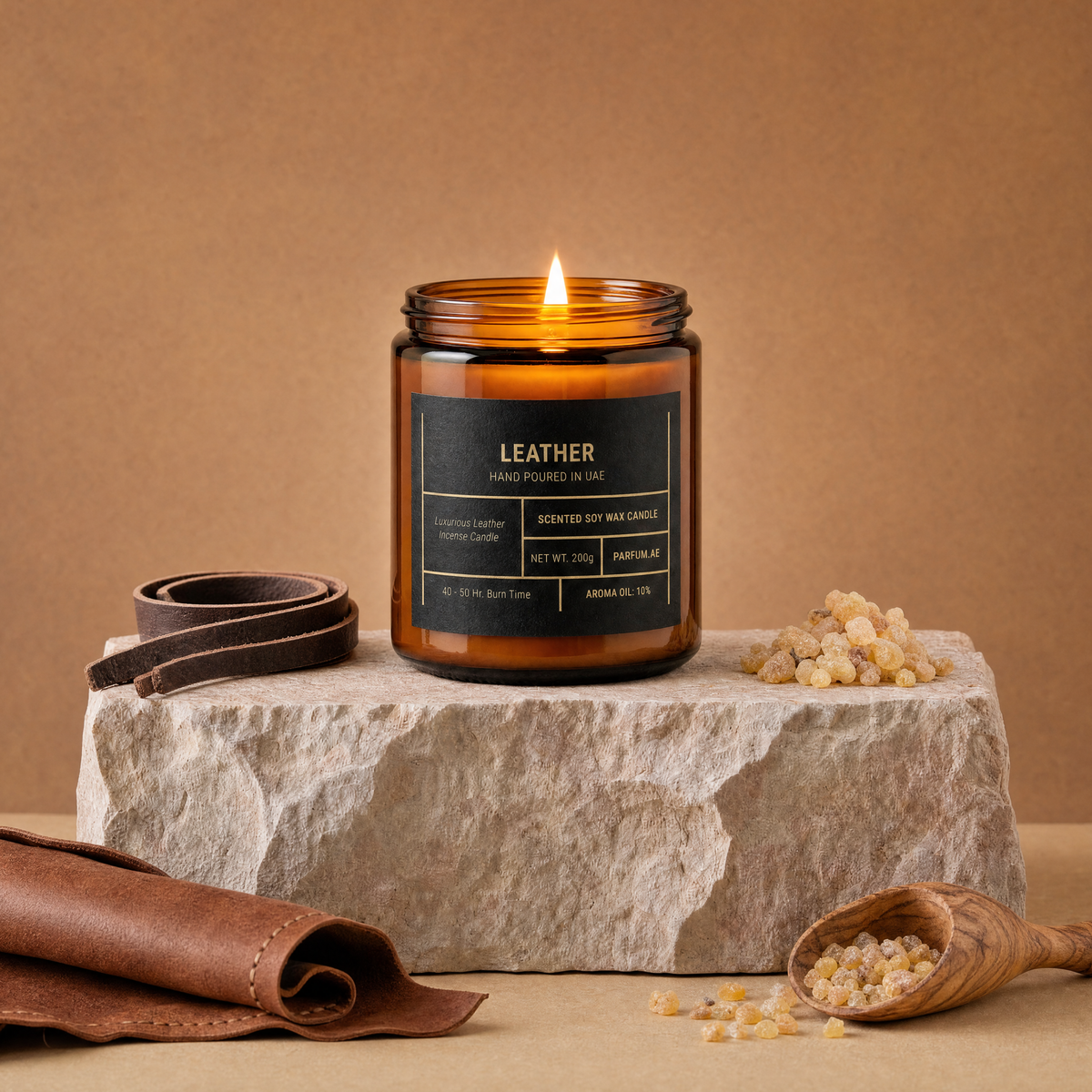 Leather scented soy wax candle, lit, on travertine stone with leather and frankincense resin